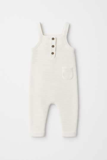 White ribbed knit overalls with button details on a light gray background
