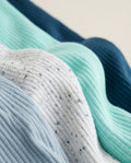 Four ribbed baby rompers on wooden hangers in grey-blue, speckled ivory, mint and navy with henley buttons and chest pockets