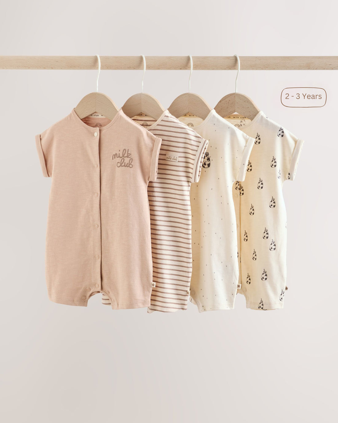 Front view of four baby rompers hanging on wooden hangers, showing the snap-front openings and short sleeves in a soft neutral colour palette.
