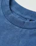 Close-up detail of a boy's blue acid wash crew neck T-shirt showing the ribbed neckline and subtle faded cotton texture.