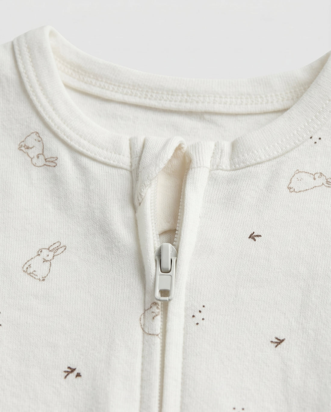Ivory baby long-sleeve zip-up romper with all-over scattered bunny and bird print in taupe, featuring front zip closure with inner guard flap and ribbed cuffs at wrists and ankles
