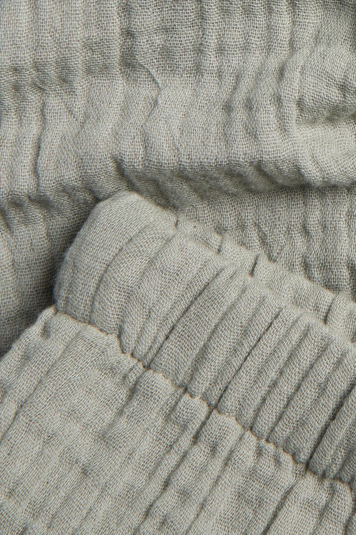 Close-up of crinkle cotton muslin fabric texture and elasticated cuff on sage green baby trousers — PTex Fashion