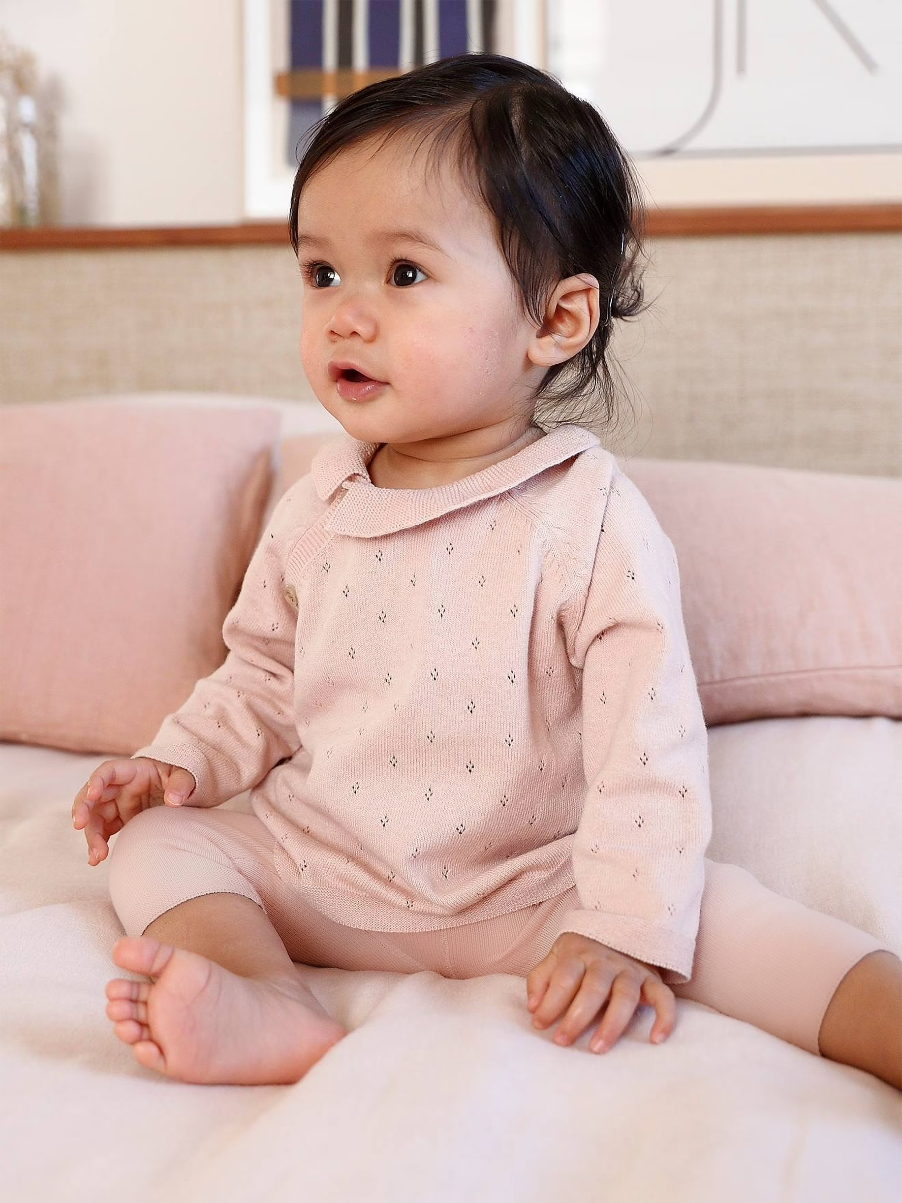 Baby in a pink outfit sitting on a couch