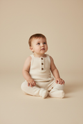 Baby wearing a white knit outfit sitting on a beige background