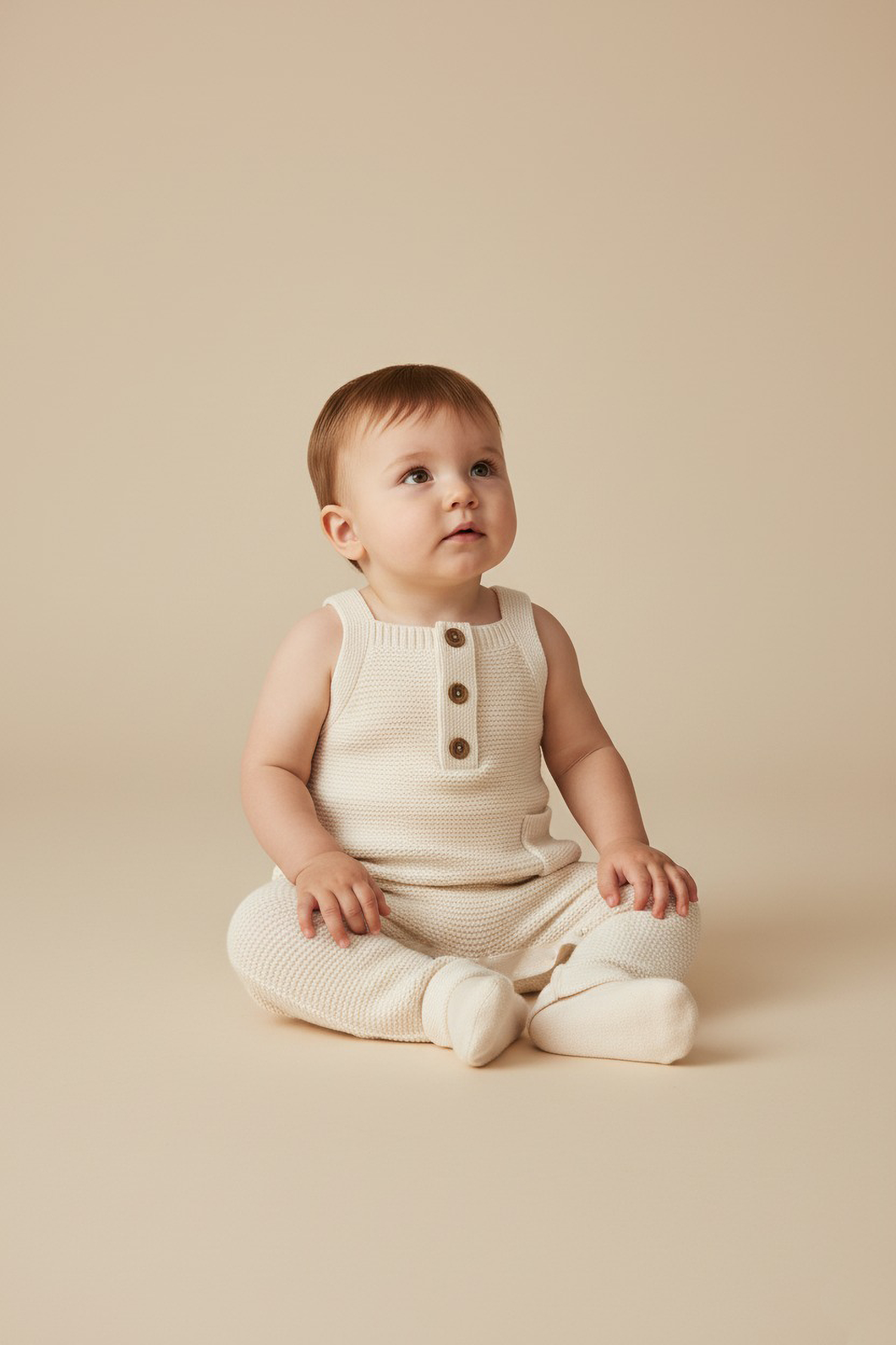 Baby wearing a white knit outfit sitting on a beige background