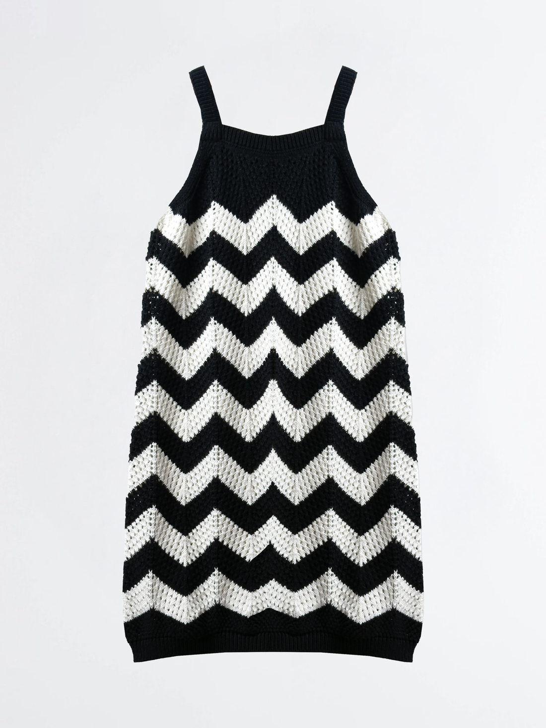 Young girl wearing a black and white zigzag dress standing in a field with greenery.