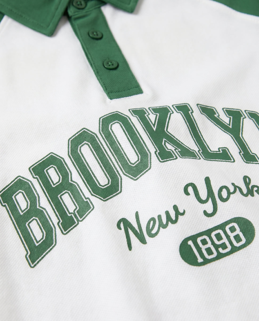 Boys' green and white raglan polo shirt with Brooklyn varsity print and striped sleeve detail, front view