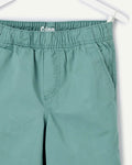 Close-up detail of boys' sage green chino shorts on white hanger, showing elastic waistband with branded interior label and front pleat construction