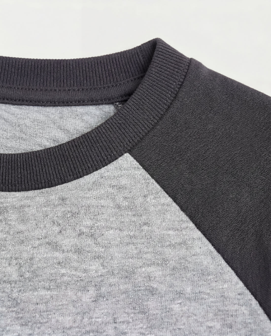Boys' short-sleeve raglan cotton t-shirt laid flat, featuring a heather grey body with contrast charcoal raglan sleeves and a ribbed crew neckline.
