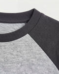 Close-up of a boys' raglan t-shirt showing a ribbed charcoal crew neckline and contrast colour-block construction with a heather grey body and dark grey raglan sleeves.