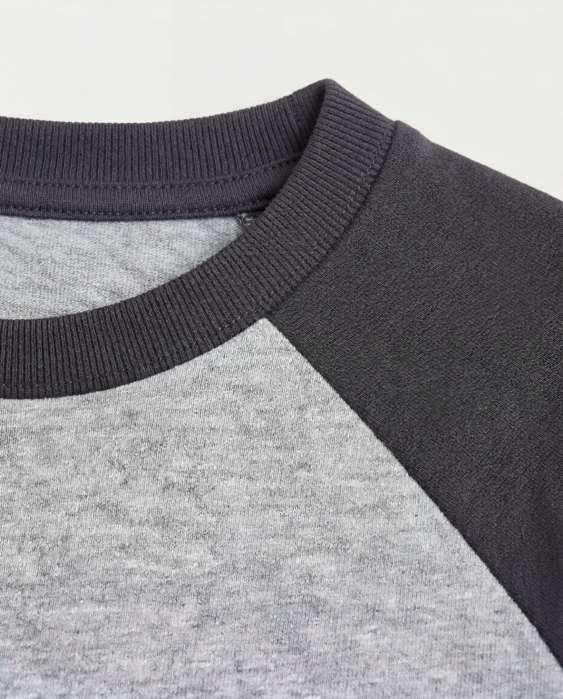 Close-up of a boys' raglan t-shirt showing a ribbed charcoal crew neckline and contrast colour-block construction with a heather grey body and dark grey raglan sleeves.