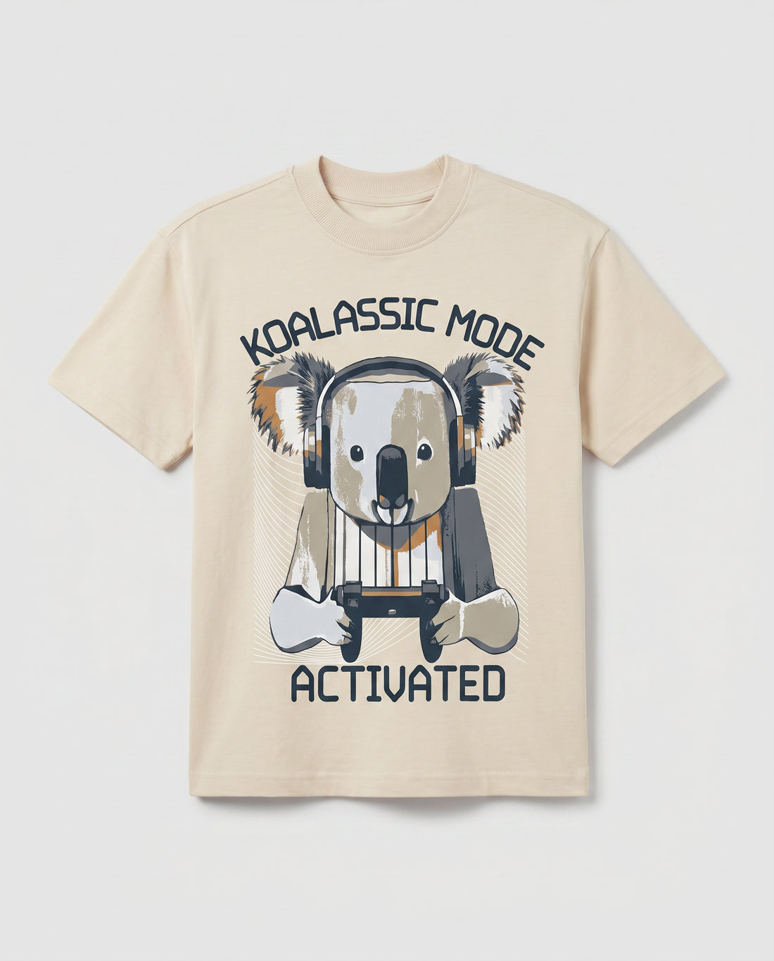 
Boys' cream-colored short-sleeve cotton t-shirt laid flat, featuring a graphic print of a cartoon koala wearing headphones and holding a gaming controller, with arched text reading "Koalassic Mode Activated" in dark navy.