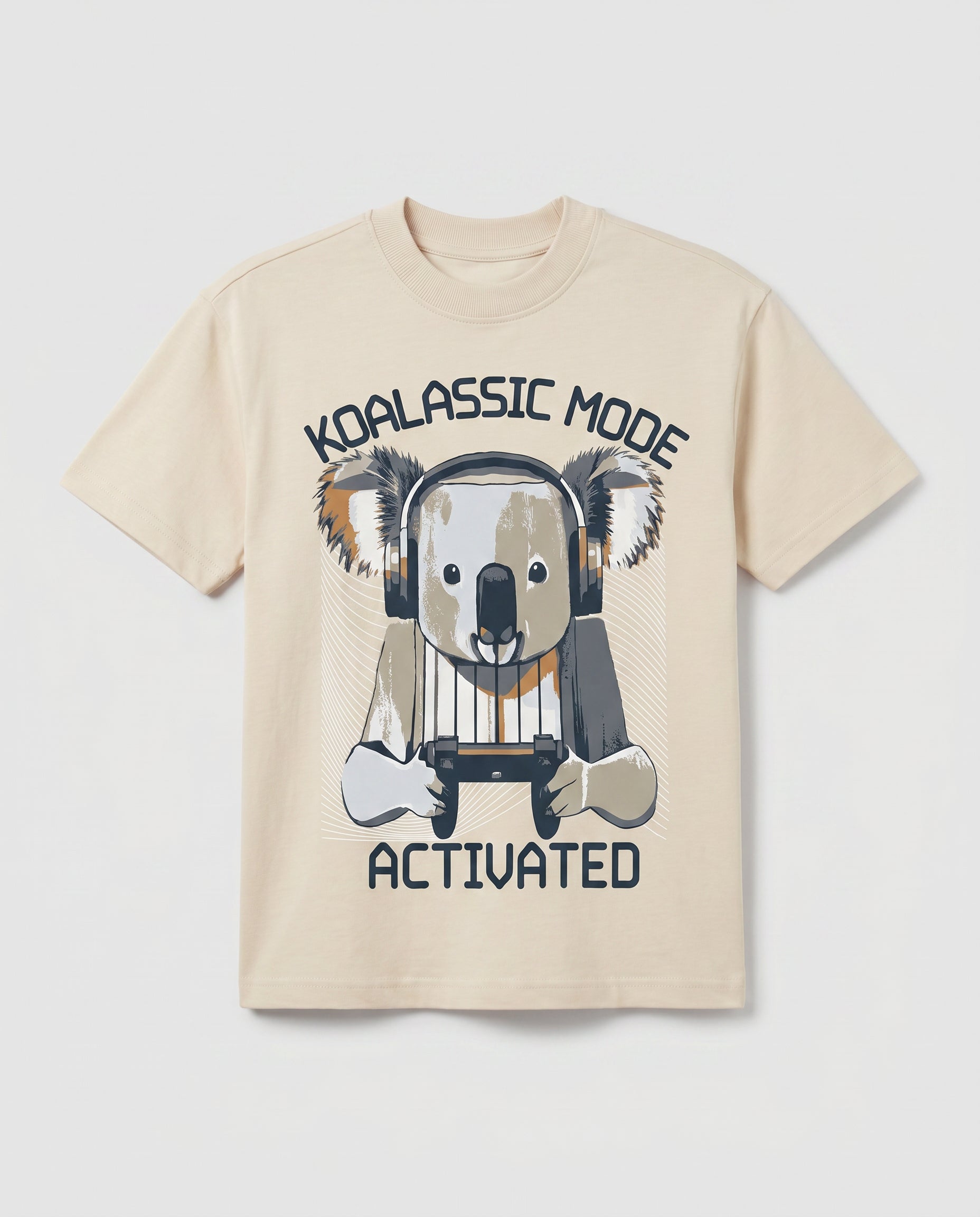 
Boys' cream-colored short-sleeve cotton t-shirt laid flat, featuring a graphic print of a cartoon koala wearing headphones and holding a gaming controller, with arched text reading "Koalassic Mode Activated" in dark navy.