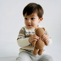 Child holding a brown knitted teddy bear against a plain background