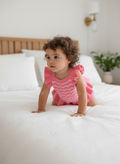 Child in a pink outfit sitting on a bed in a bedroom setting