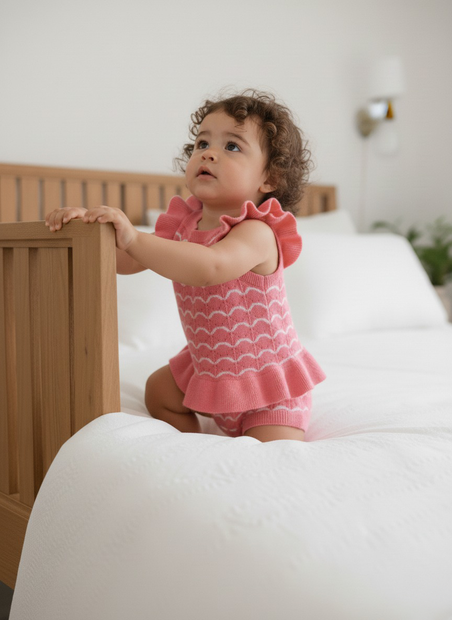 Child in a pink outfit standing on a bed