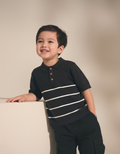 Child wearing a black polo shirt with white stripes against a beige background