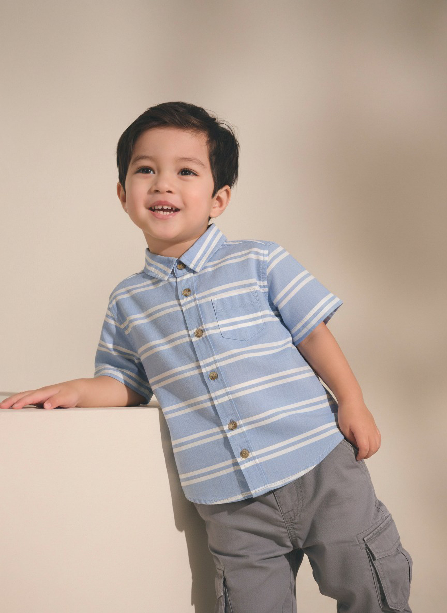 Child wearing a blue striped shirt and gray pants against a beige background