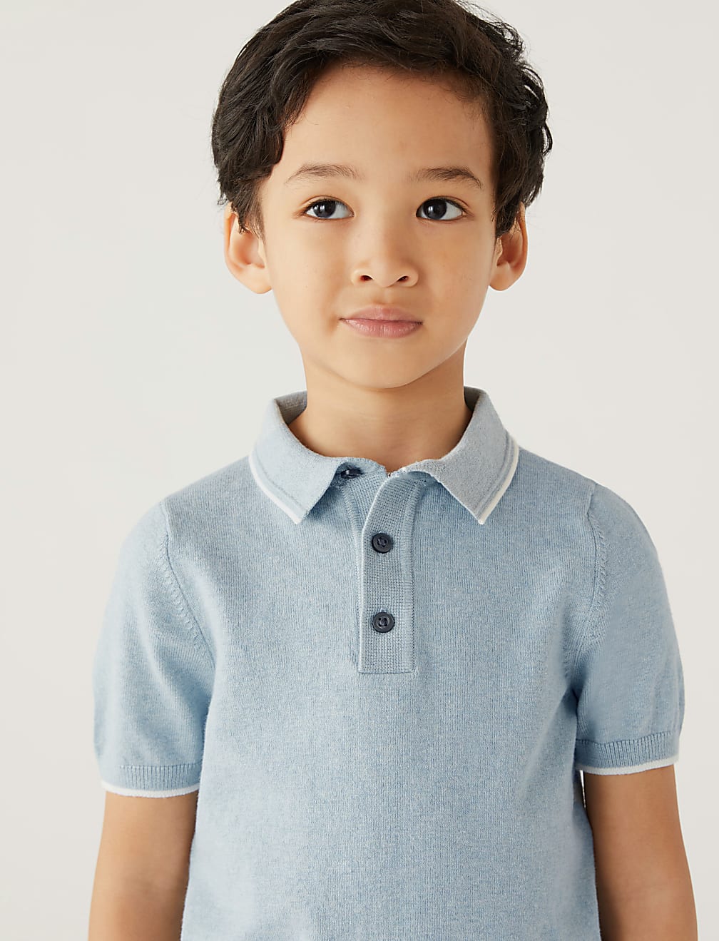 Child wearing a light blue polo shirt with a white collar against a plain background