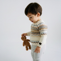 Child wearing a patterned sweater holding a teddy bear against a plain background