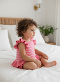 Child wearing a pink outfit sitting on a bed in a bedroom.