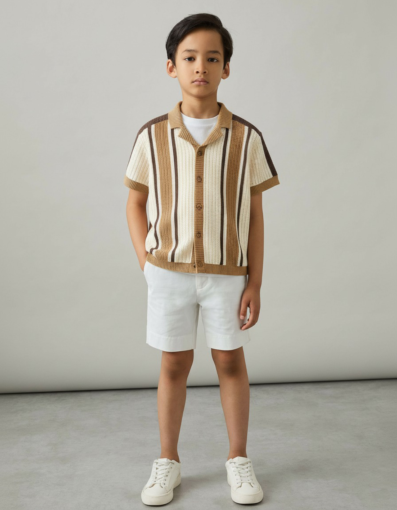 Child wearing a striped shirt and white shorts against a plain background