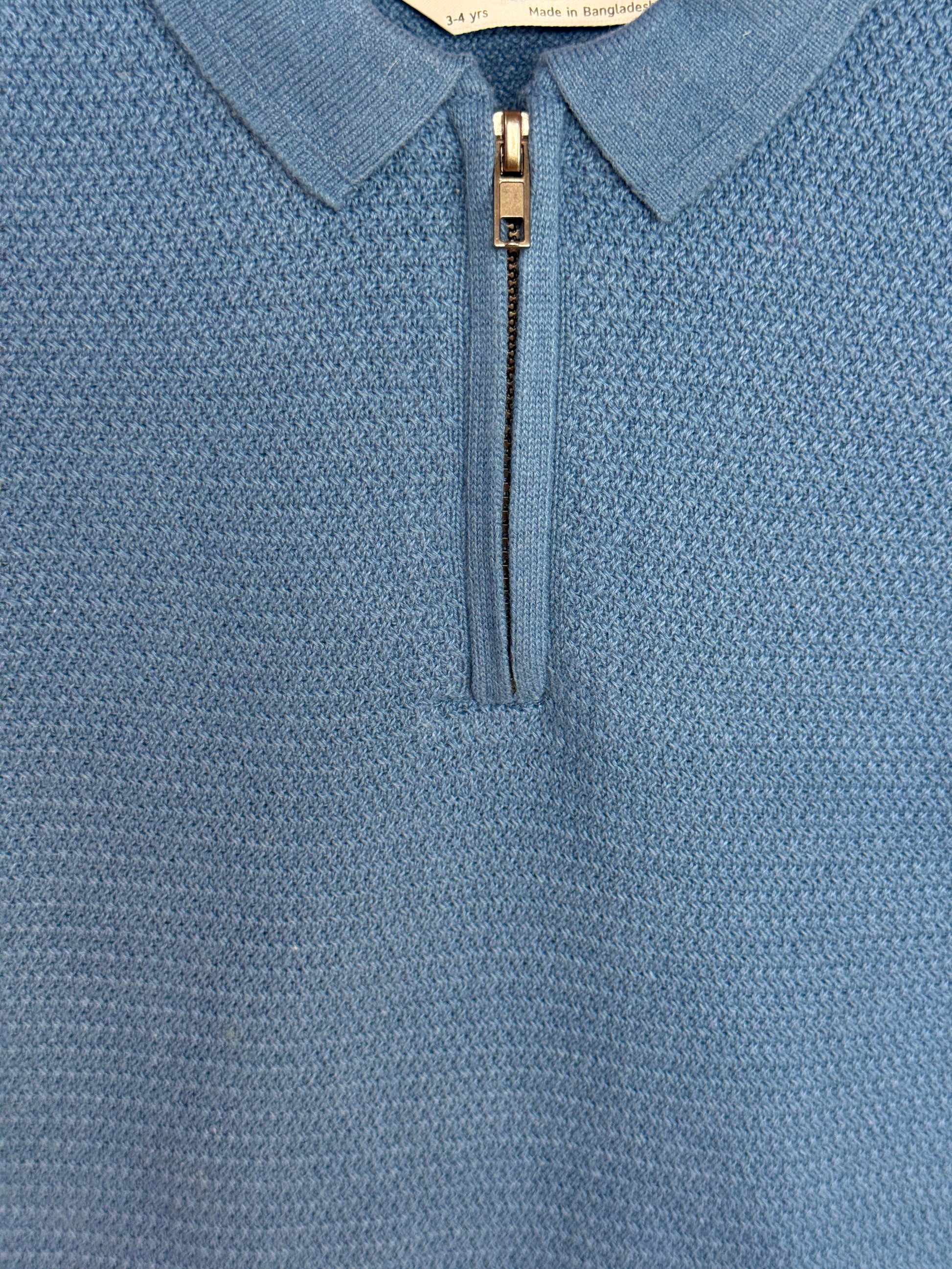 Close-up of a blue textured polo shirt with a zipper detail.