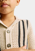 Close-up of a child wearing a beige knitted polo with black stripes on a light background