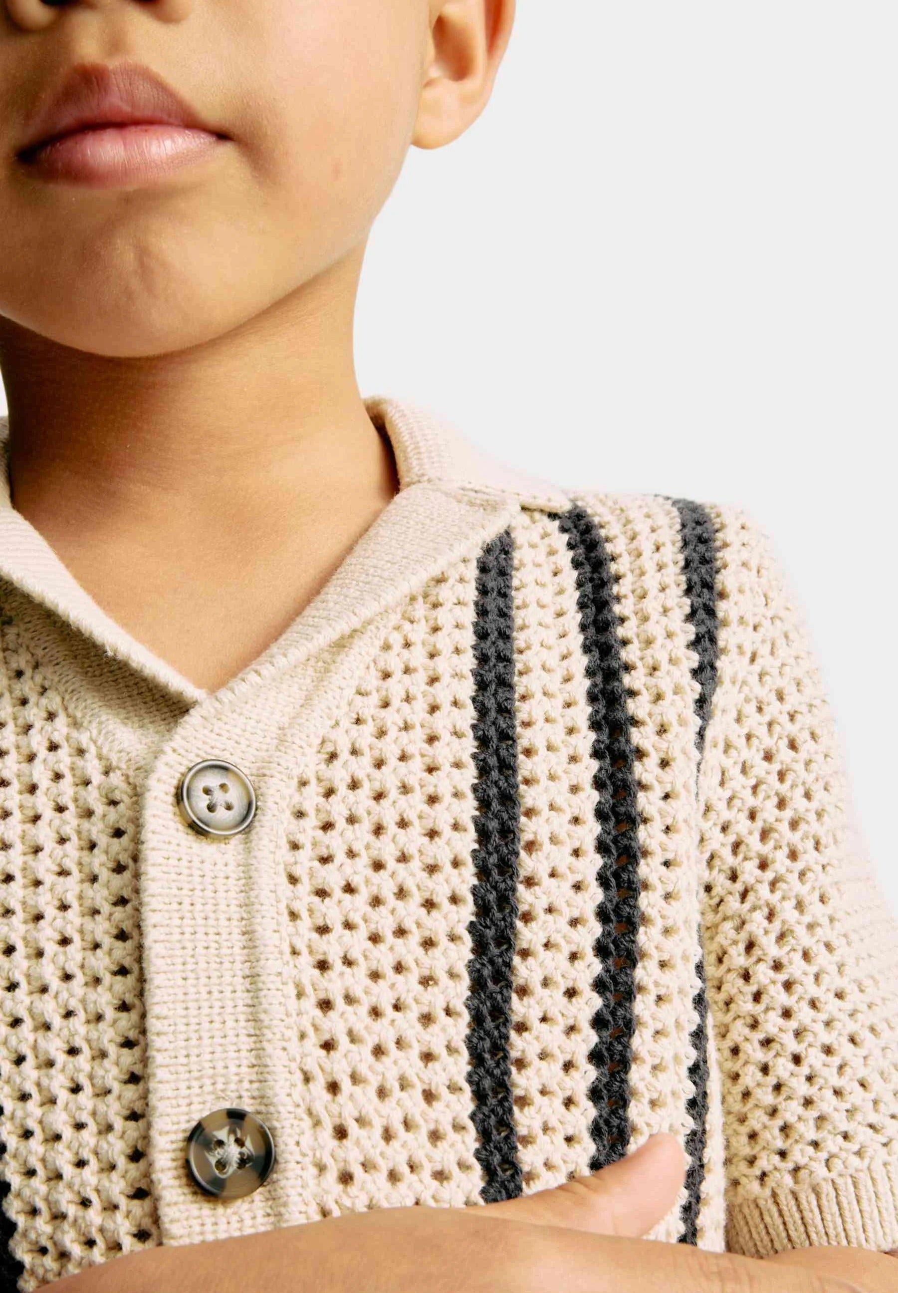 Close-up of a child wearing a beige knitted polo with black stripes on a light background
