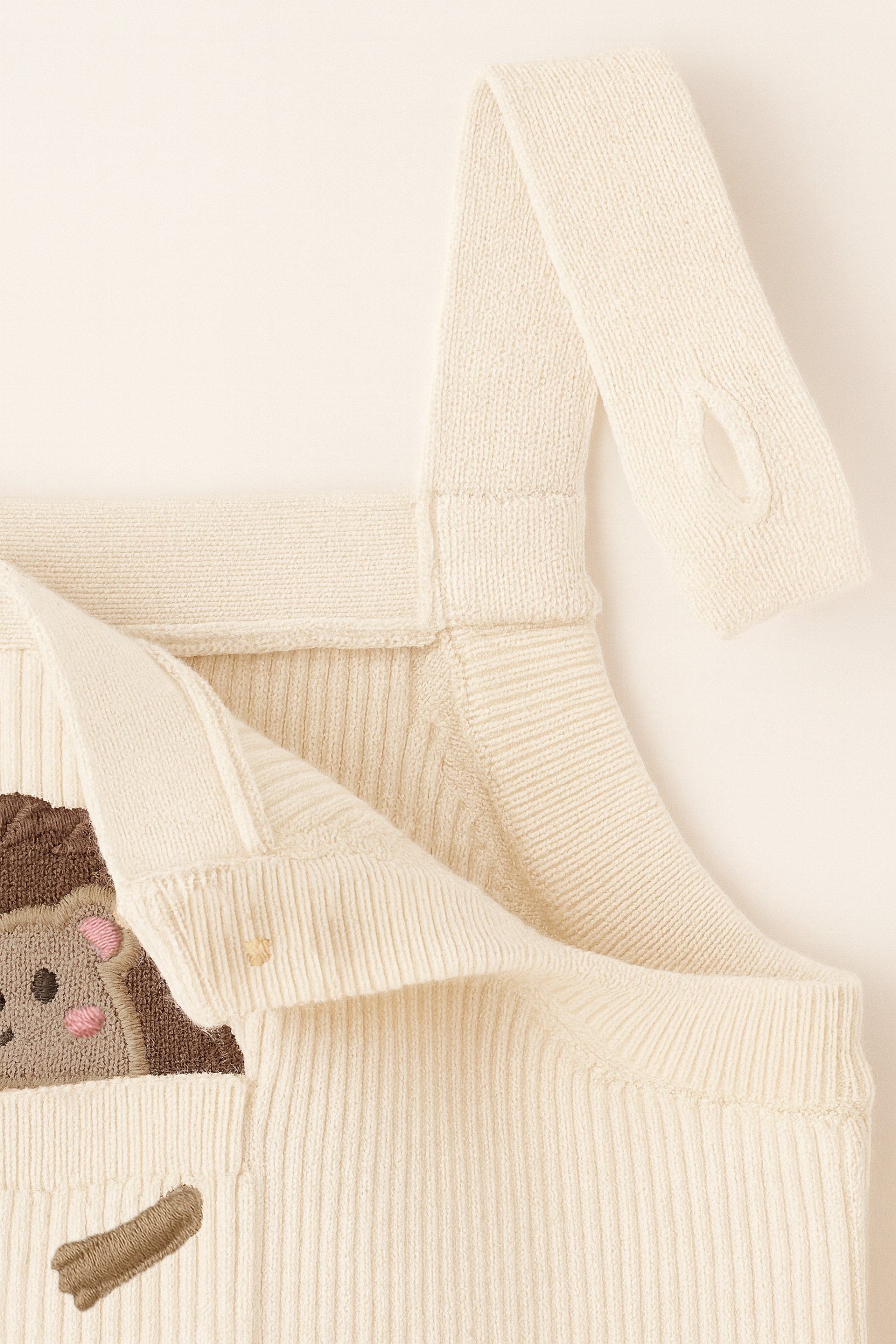 Close-up of a cream-colored knit garment with a small animal design on a light background
