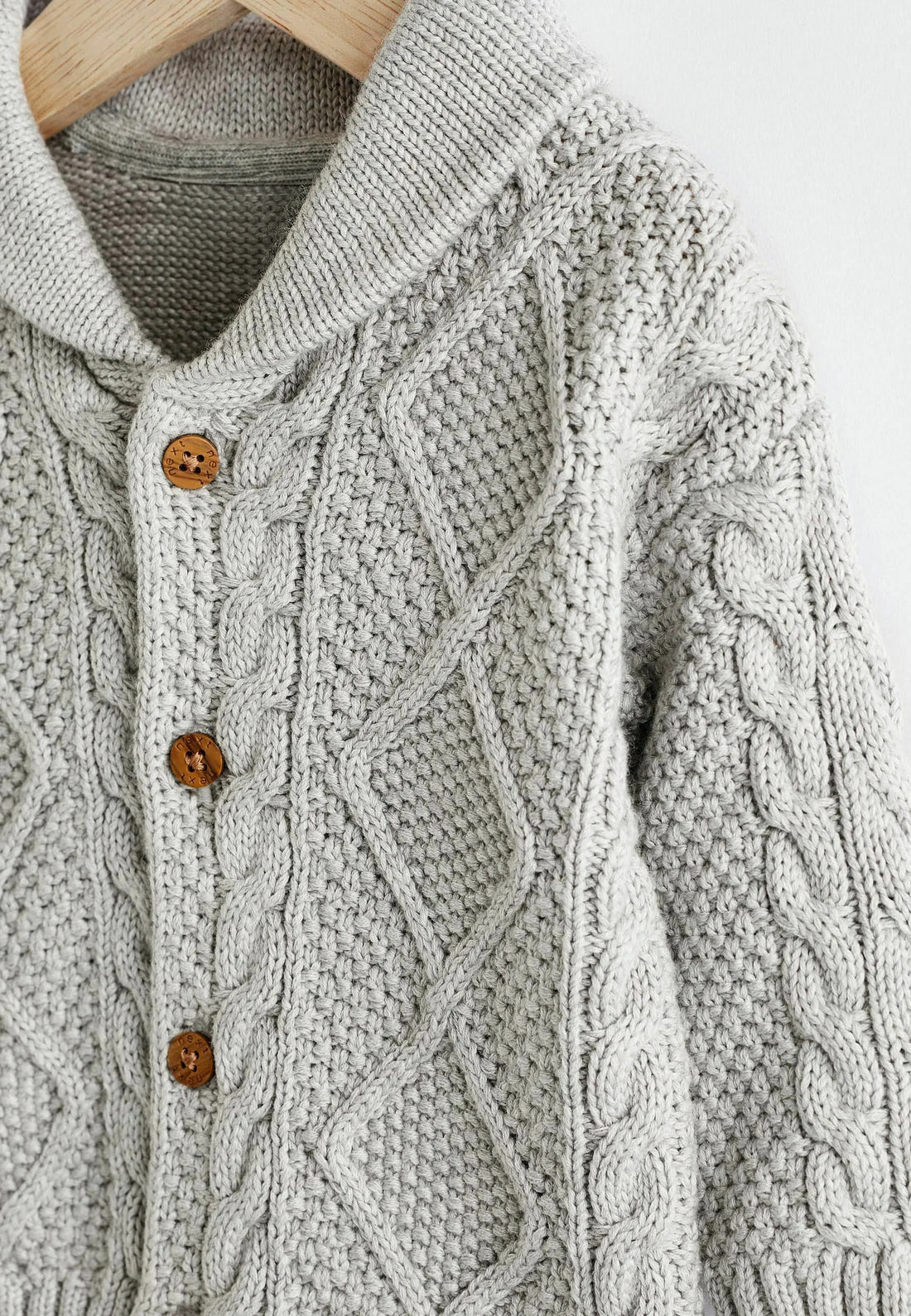 Knitted baby cardigan on a hanger against a white background