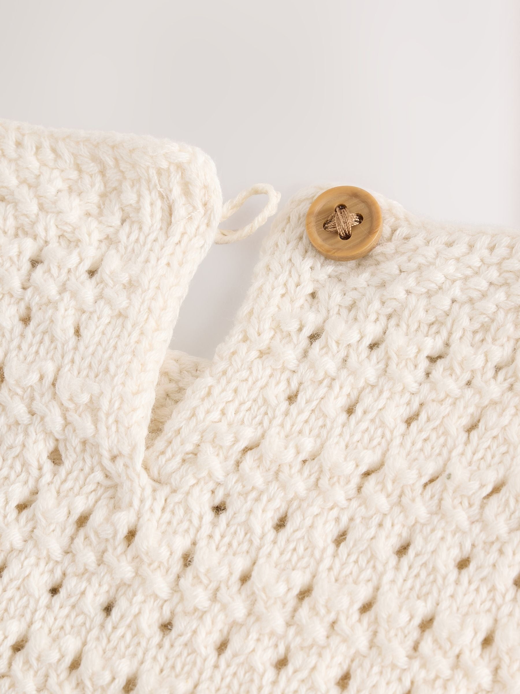 Close-up of a knitted cream-colored garment with a wooden button on a light gray background