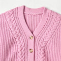 Close-up of a pink knitted cardigan with cable pattern and gold buttons on a light gray background