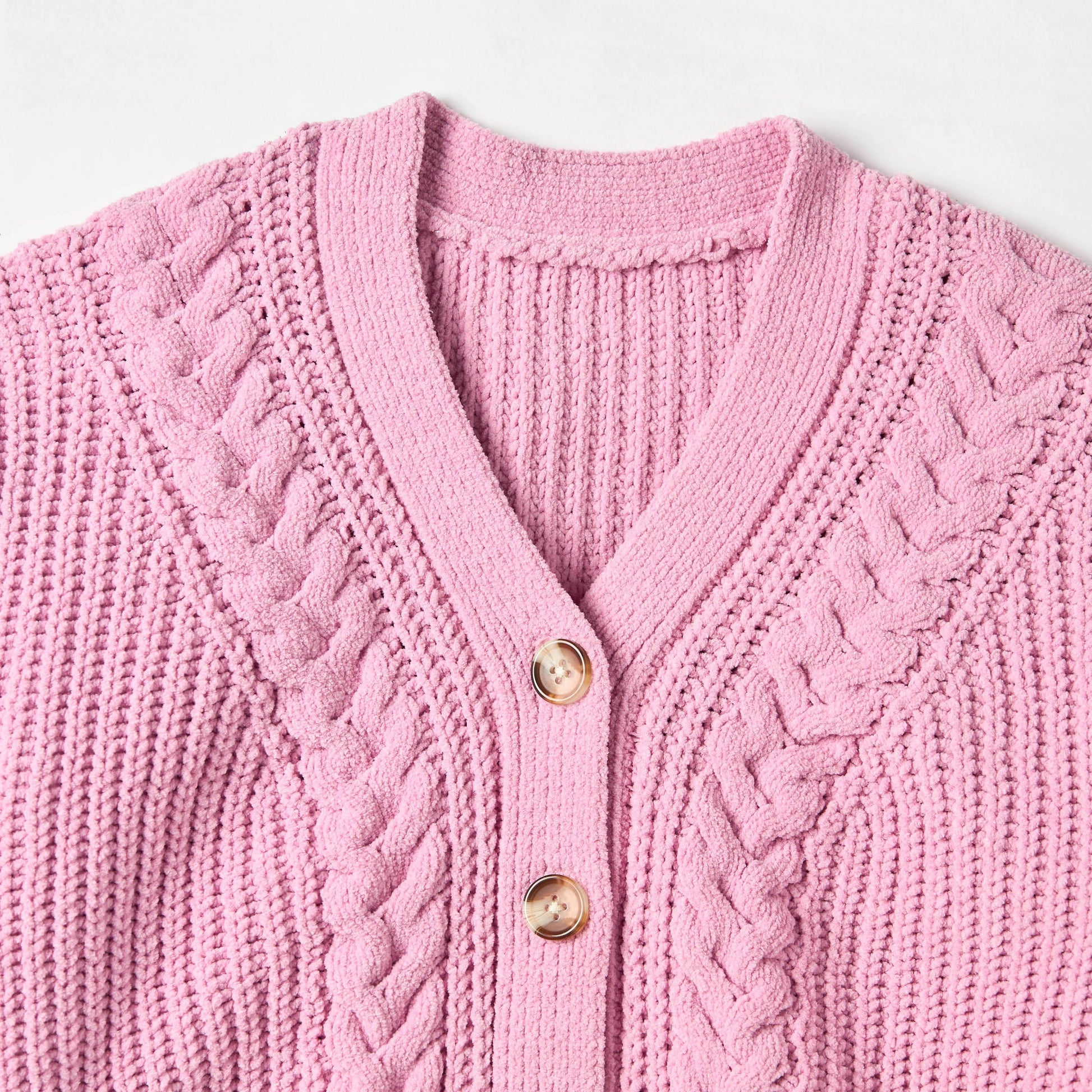 Close-up of a pink knitted cardigan with cable pattern and gold buttons on a light gray background