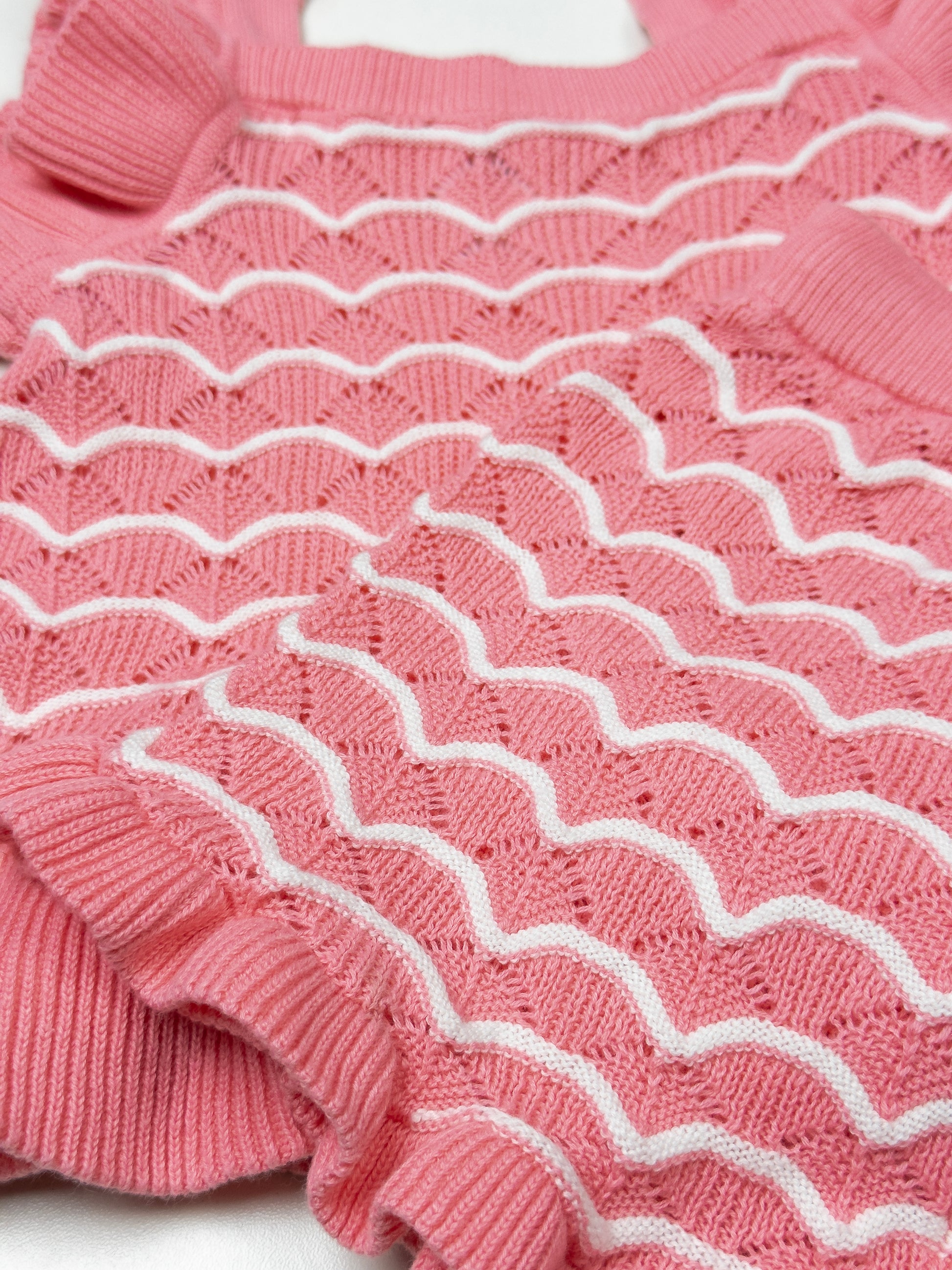 Close-up of a pink knitted garment with white ribbing on a white background