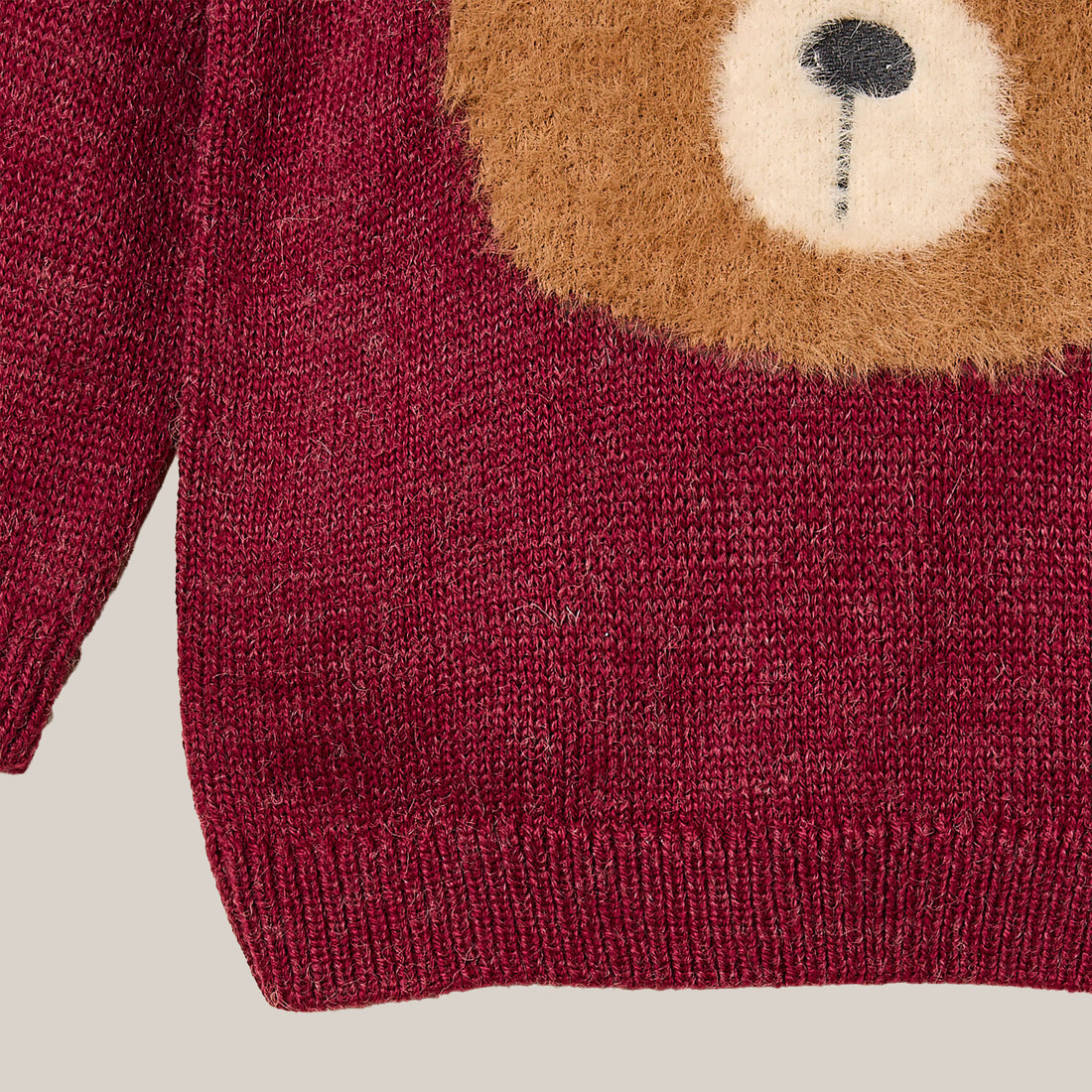 Red sweater with a bear face design on a wooden hanger against a white background