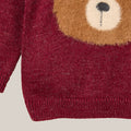 Close-up of a red knitted sweater with a bear face design on a light gray background