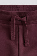 Close-up of maroon sweatpants with a drawstring on a light gray background