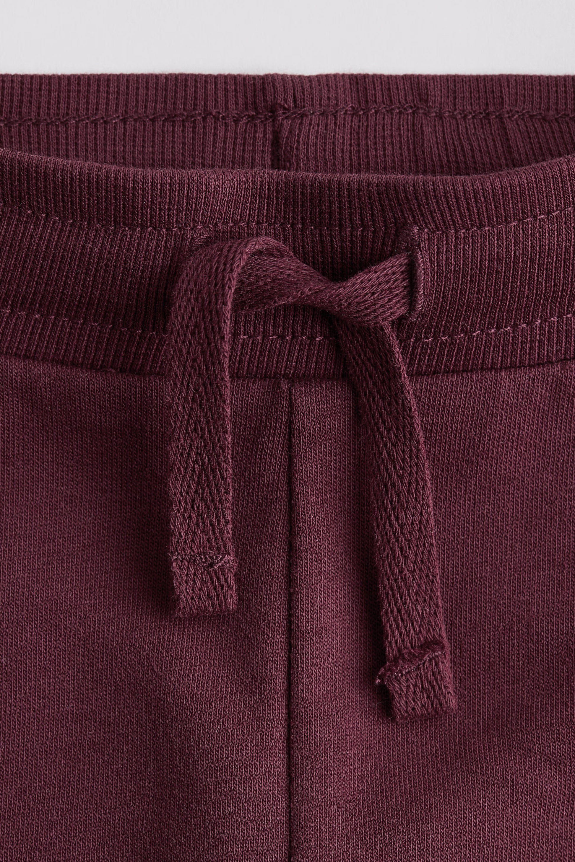 Close-up of maroon sweatpants with a drawstring on a light gray background