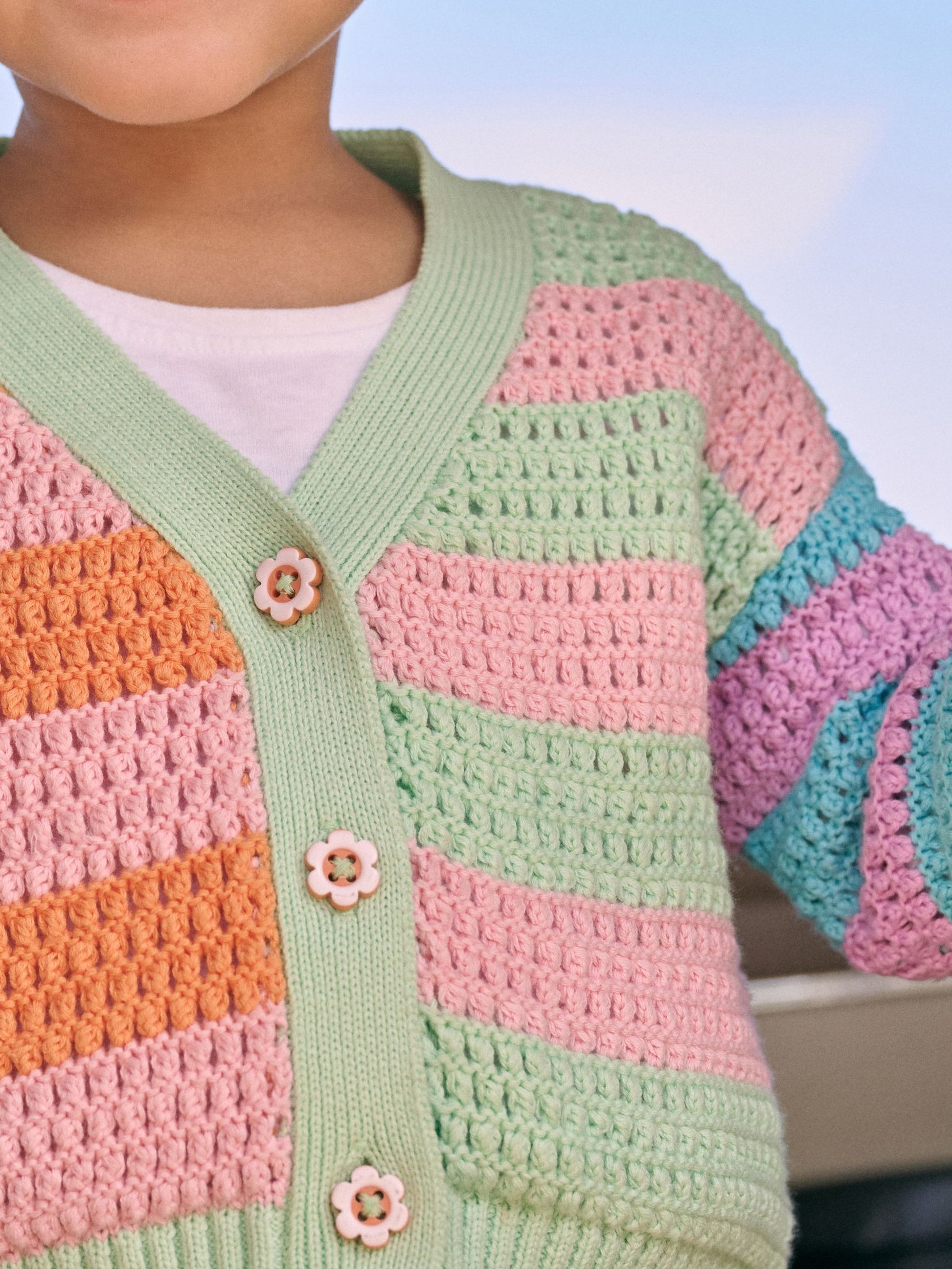 Colorful crocheted cardigan with flower buttons on a blurred background