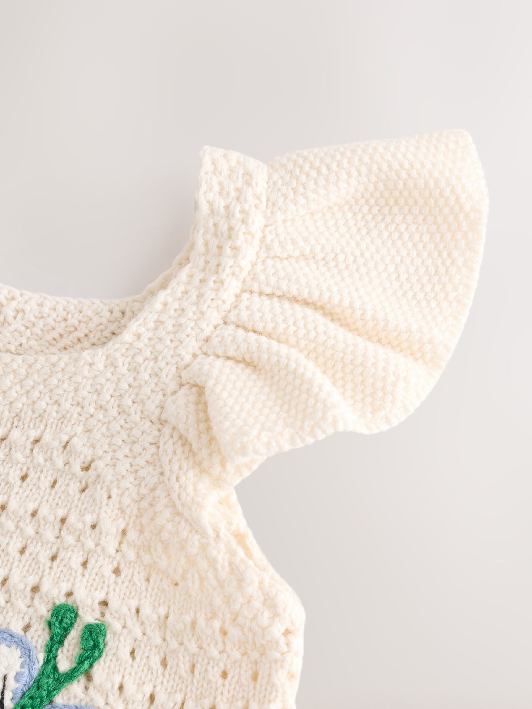 Cream-colored knitted dress with ruffled collar on a light gray background