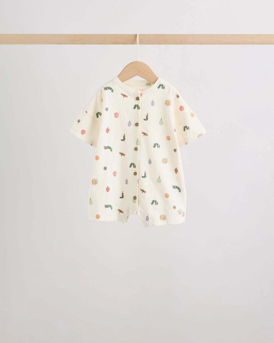 Cream all-over print baby romper with scattered caterpillar and fruit motifs, wooden button front placket, on wooden hanger

