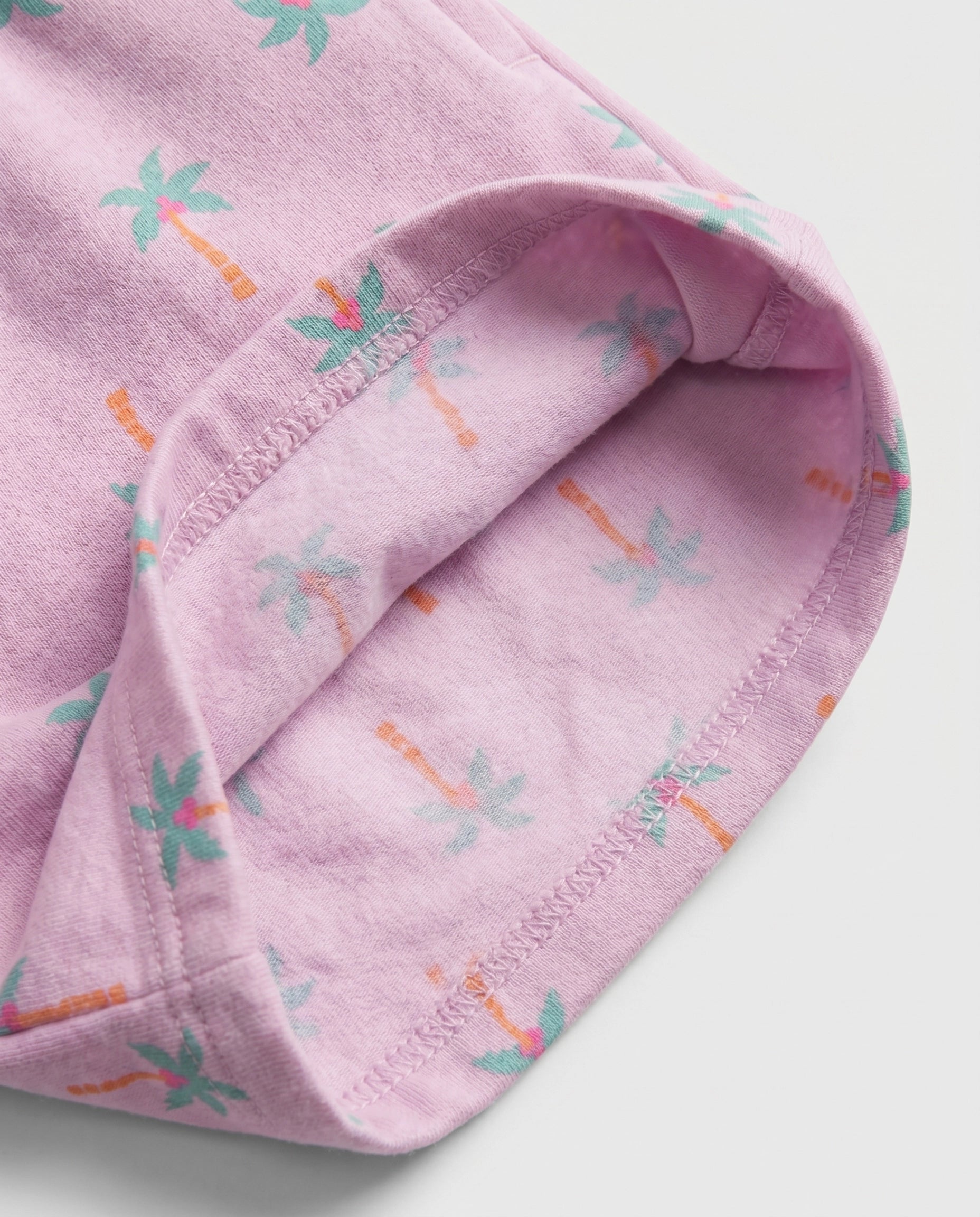 Close-up of lilac palm tree print cotton fabric showing matching soft printed cotton inner lining and overlock stitch hem detail of girl's short pant
