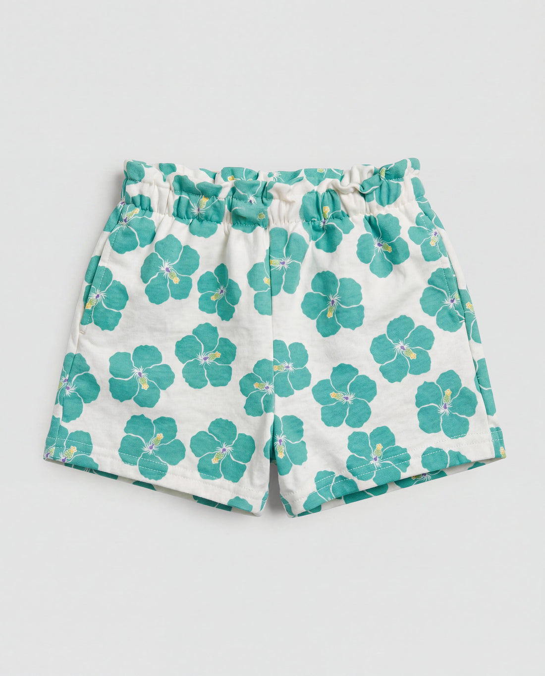 Front flat-lay view of girl's white short pant with bold teal hibiscus all-over print and paperbag elasticated waistband