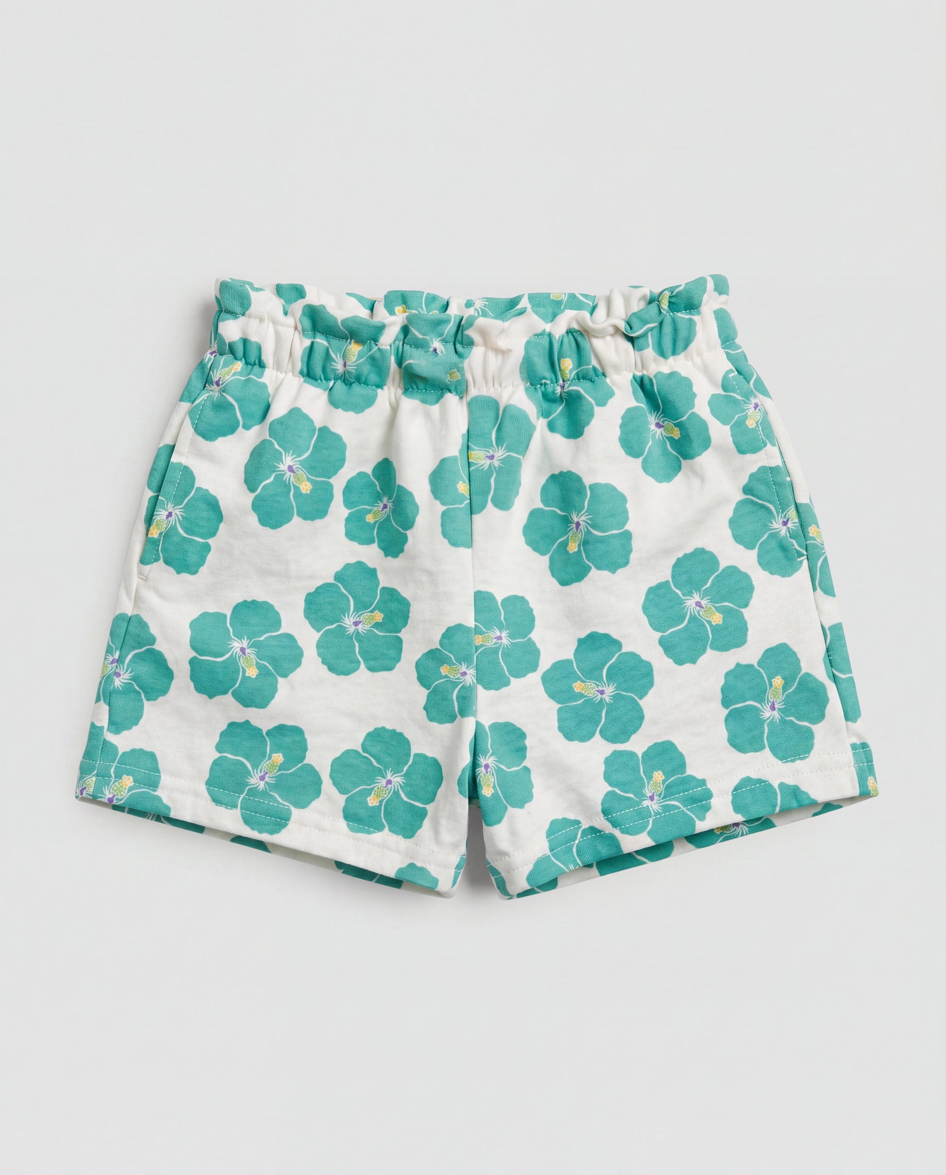 Front flat-lay view of girl's white short pant with bold teal hibiscus all-over print and paperbag elasticated waistband