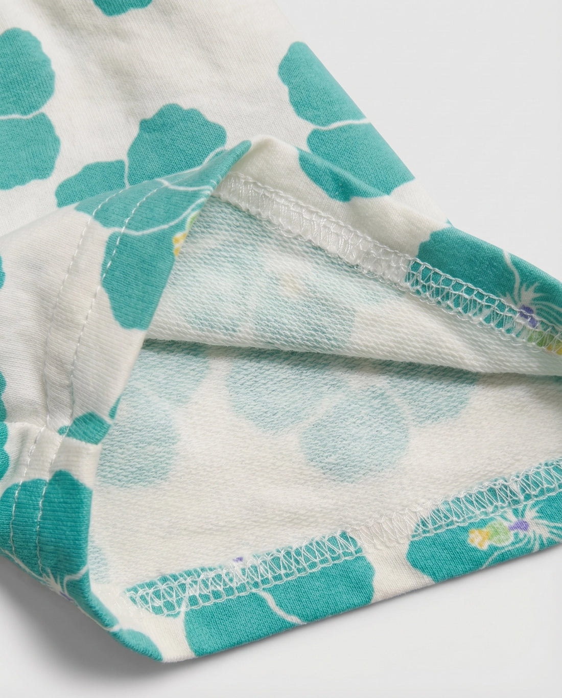 Front flat-lay view of girl's white short pant with bold teal hibiscus all-over print and paperbag elasticated waistband