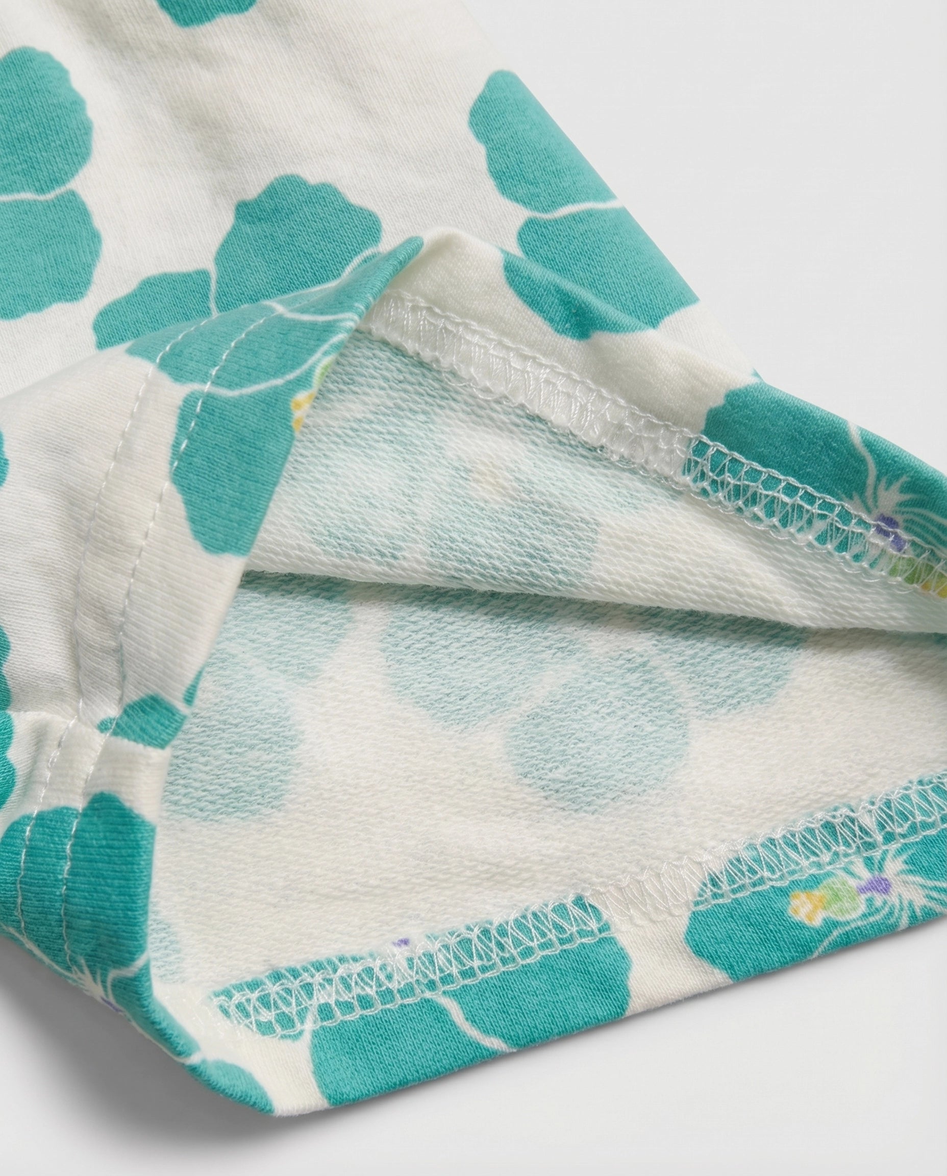 Close-up of white and teal hibiscus print cotton fabric showing soft brushed cotton terry inner lining and overlock stitch finishing detail