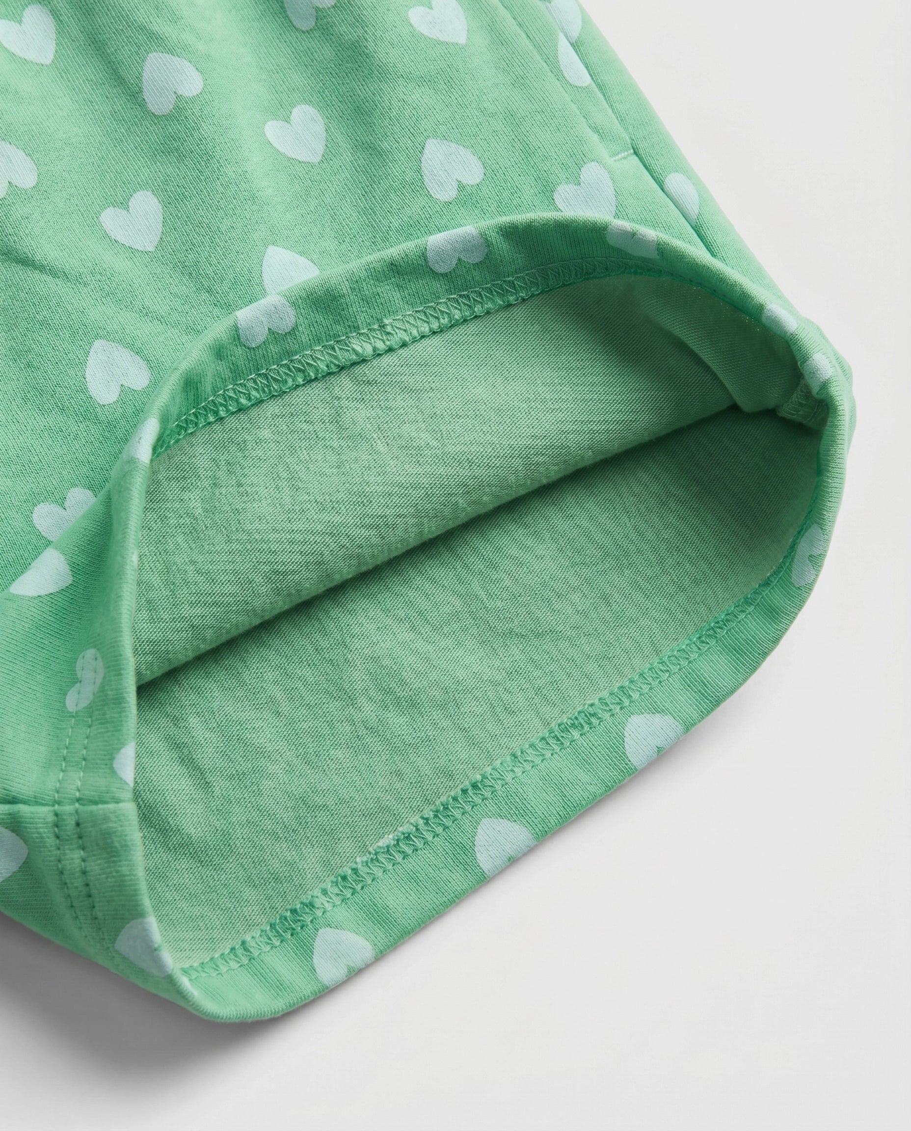 Close-up of green heart print cotton fabric showing matching soft green cotton inner lining and overlock stitch hem detail of girl's short pant
