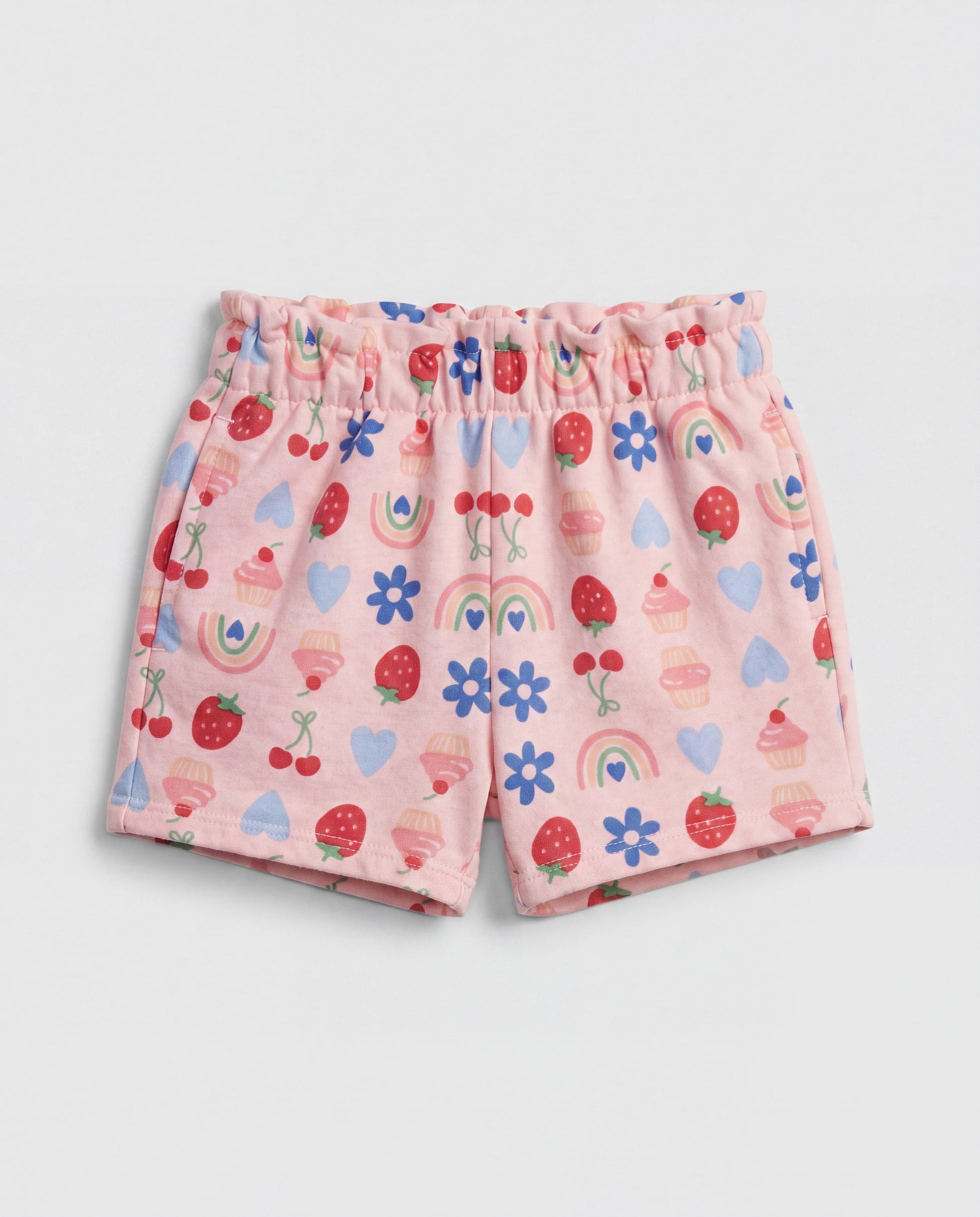 Front flat-lay view of girl's blush pink short pant with all-over multicolour strawberry, cherry, cupcake, rainbow, daisy and heart print and ruched paperbag elasticated waistband