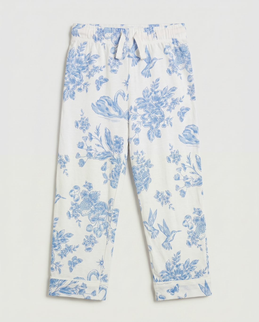 Full flat lay front view:
Girls' pyjama pants in ivory with an all-over blue toile de Jouy print featuring hummingbirds, swans, strawberries, and floral motifs, displayed flat lay on a white background with a relaxed straight leg and folded cuff hem.